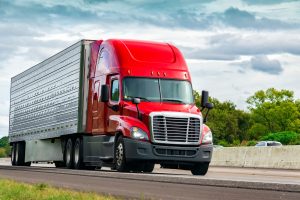 Red semi-truck driving on highway for interstate truck registration and delivery services