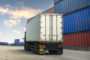 Truck parked near shipping containers for port-to-dealer logistics services